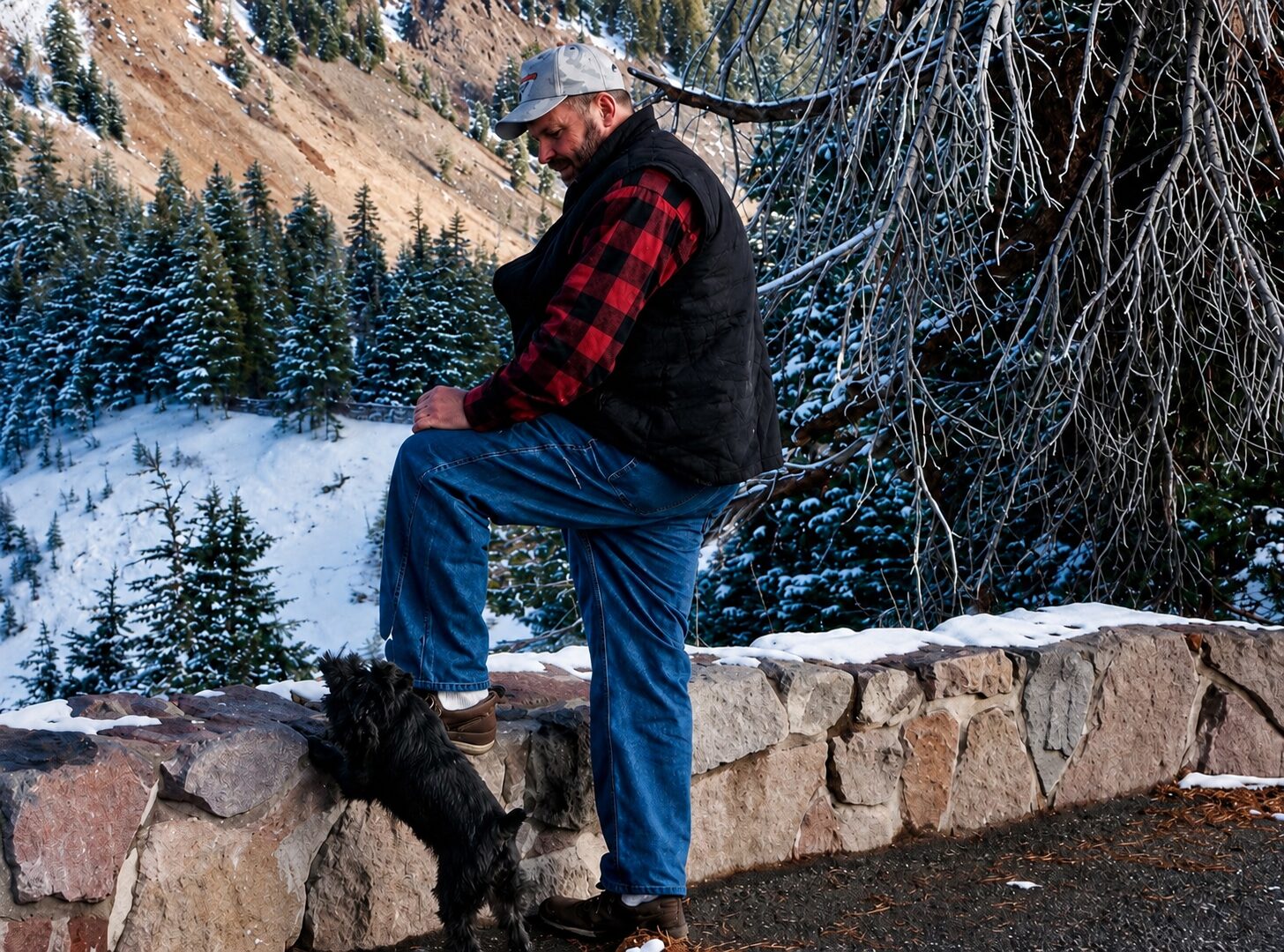 John Cox with his schnauzer Maggie Mae on a stone wall in the mountains